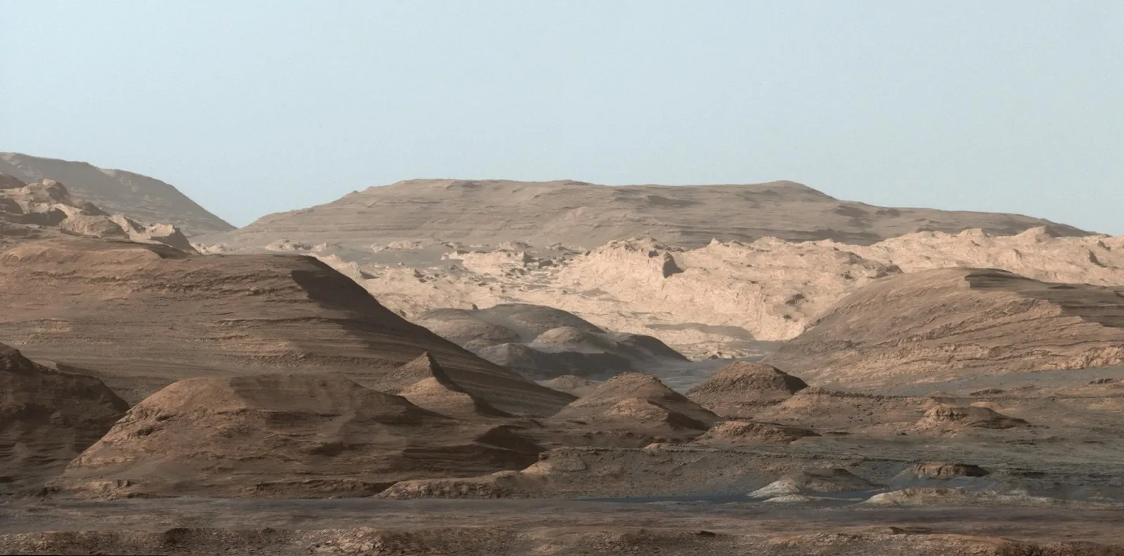 Layered buttes and pale rock outcrops on Mount Sharp, Mars, under a hazy sky. Image: NASA/JPL-Caltech/MSSS